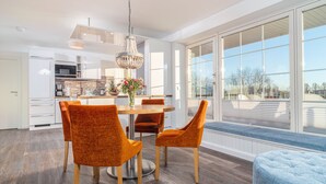 A modern kitchen with white cabinetry, a dining area with orange chairs, and large windows offering a view of the outdoors. - Vacation apartment Inga in the Ostseebad Dierhagen (Dierhagen)
