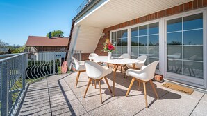 A covered outdoor patio with a round table and white chairs, a flower arrangement, and a view of the neighborhood. - Vacation apartment Inga in the Ostseebad Dierhagen (Dierhagen)