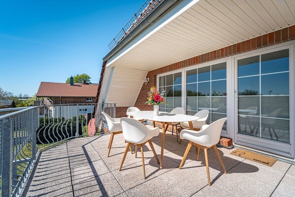 A covered outdoor patio with a round table and white chairs, a flower arrangement, and a view of the neighborhood. - Inga Vacation Apartment in Ostseebad Dierhagen (Dierhagen)