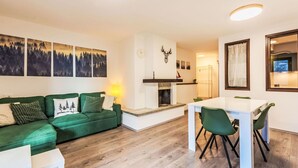 A modern living room with a green sofa, a white coffee table, and a dining area with a white table and green chairs. - Lovely apartment for 4 people with A/C, WIFI, TV and terrace (Giustino)