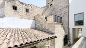 A courtyard with a tiled roof, stone walls, and a small balcony with a railing.