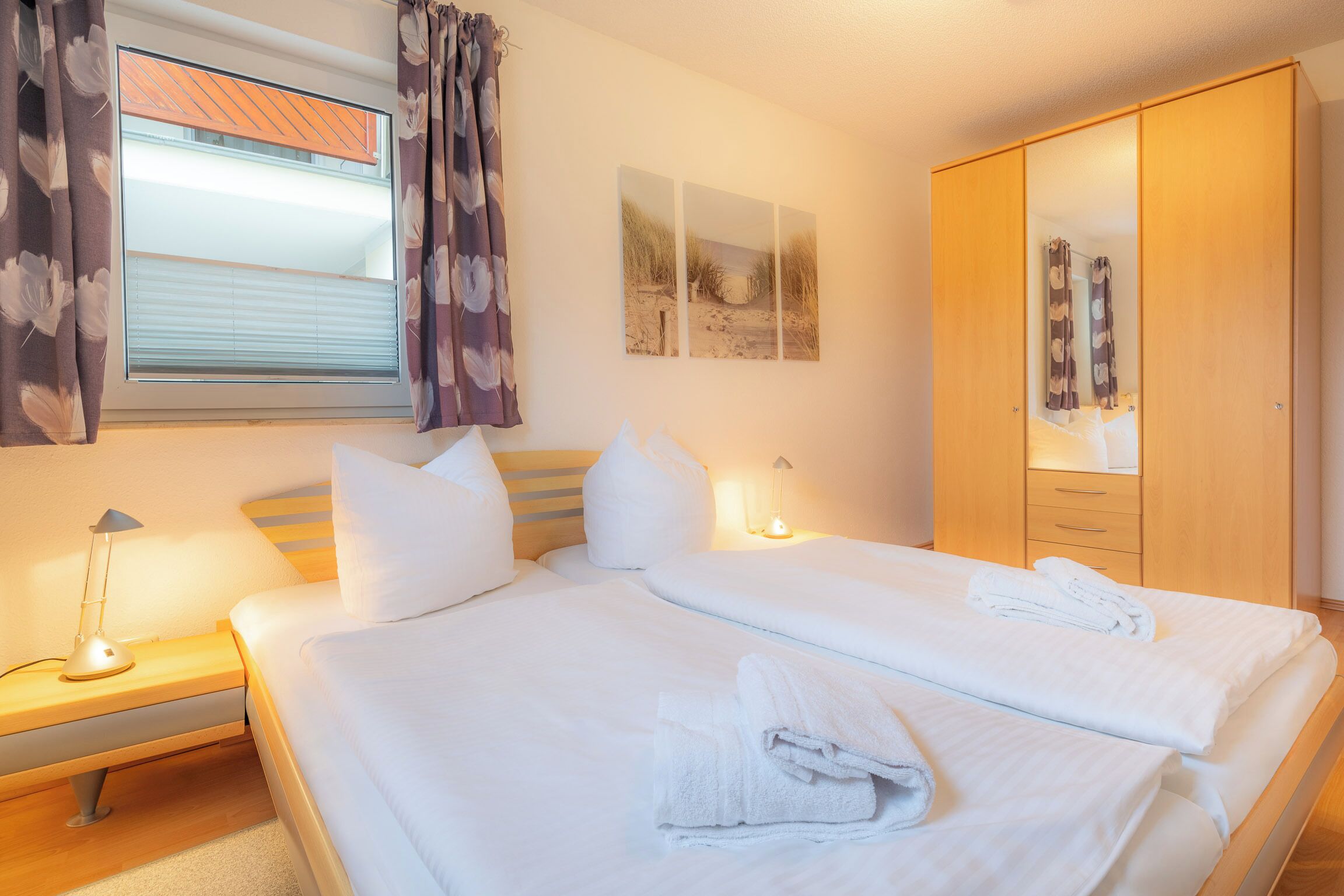 A hotel room with two beds, a wardrobe, a nightstand, and a window with curtains.