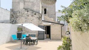 A courtyard with a table and chairs under a white umbrella, surrounded by stone walls and potted plants. - Cosy apartment for 4 guests with A/C, TV, patio and pets allowed (Morciano Di Leuca)