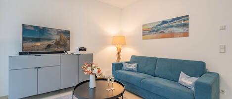 Una sala de estar moderna con un sofá azul, un mueble gris, una mesa de centro redonda y dos cuadros en la pared.