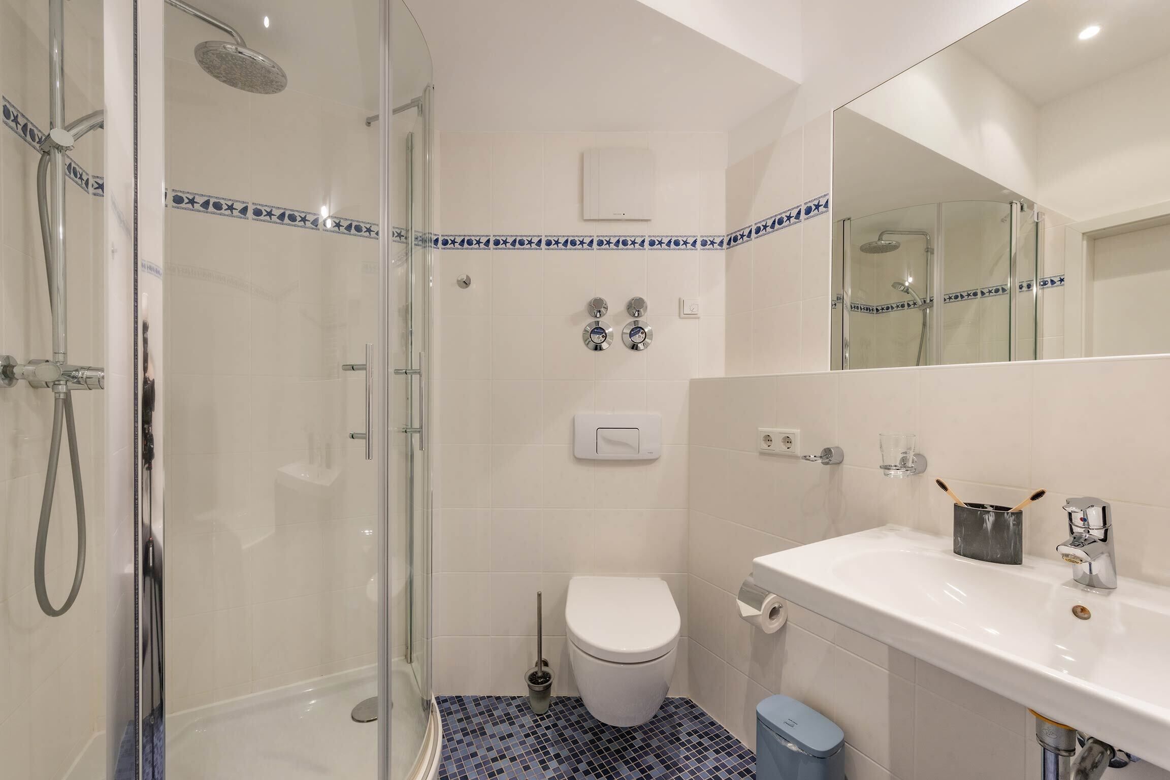 Une salle de bain avec une douche à parois de verre, des toilettes blanches et un lavabo avec un miroir.
