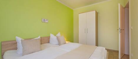 A neatly made bed with white linens and beige pillows, a white wardrobe, and a green wall.