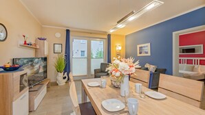 Un espace repas moderne avec une table en bois dressée pour quatre personnes, un téléviseur et une plante en pot.