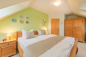 A bedroom with a large bed, wooden nightstands, a wardrobe, and a green wall with wall art. - Görmitz 36 - 12 Eulennest: An oasis of well-being in Zinnowitz with a sauna and fireplace (Zinnowitz)