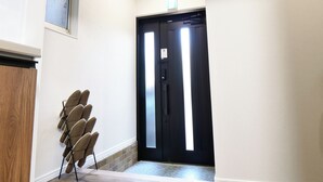 A hallway with a black door, a shoe rack, and a tiled floor. - TE HOUSE Osaka-Tennoji (Osaka)