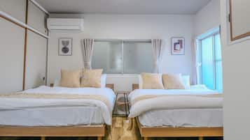 Two single beds with white bedding, a wooden desk, and a large window with curtains.