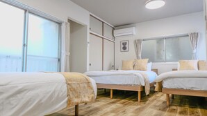 A hotel room with three single beds, wooden flooring, a large window with curtains, an air conditioning unit, and a ceiling light. - TE HOUSE Osaka-Tennoji (Osaka)