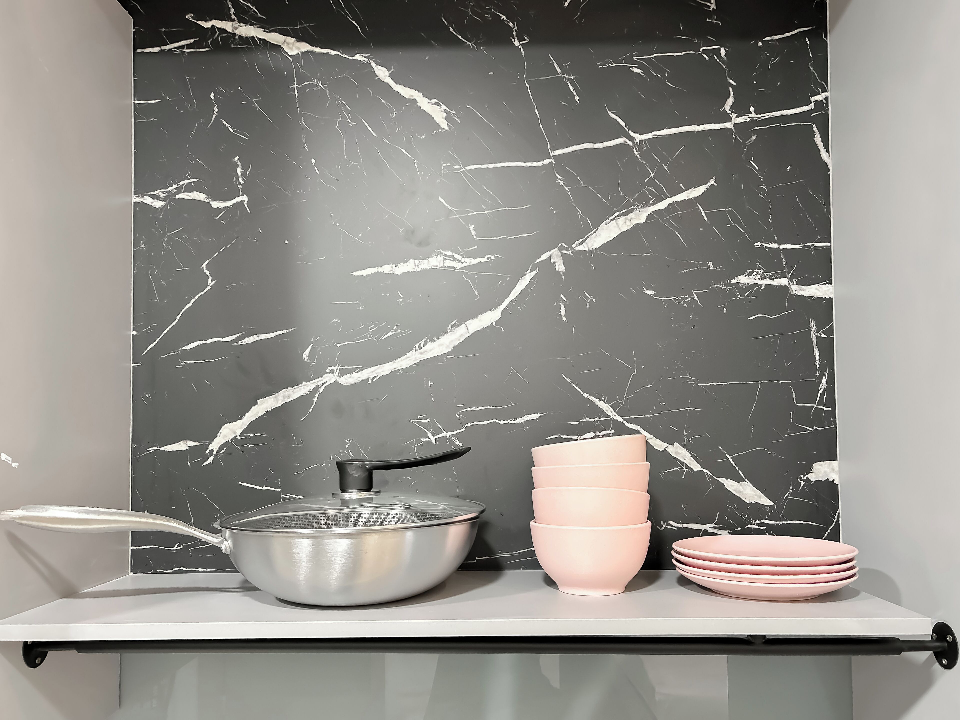 A kitchen with a marble backsplash, a stainless steel pot on the stove, and pink bowls stacked on the counter.