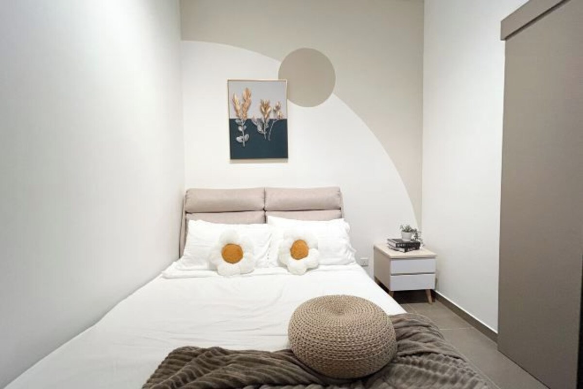 Un dormitorio ordenado con una cama, almohadas, una mesita de noche y una obra de arte en la pared.