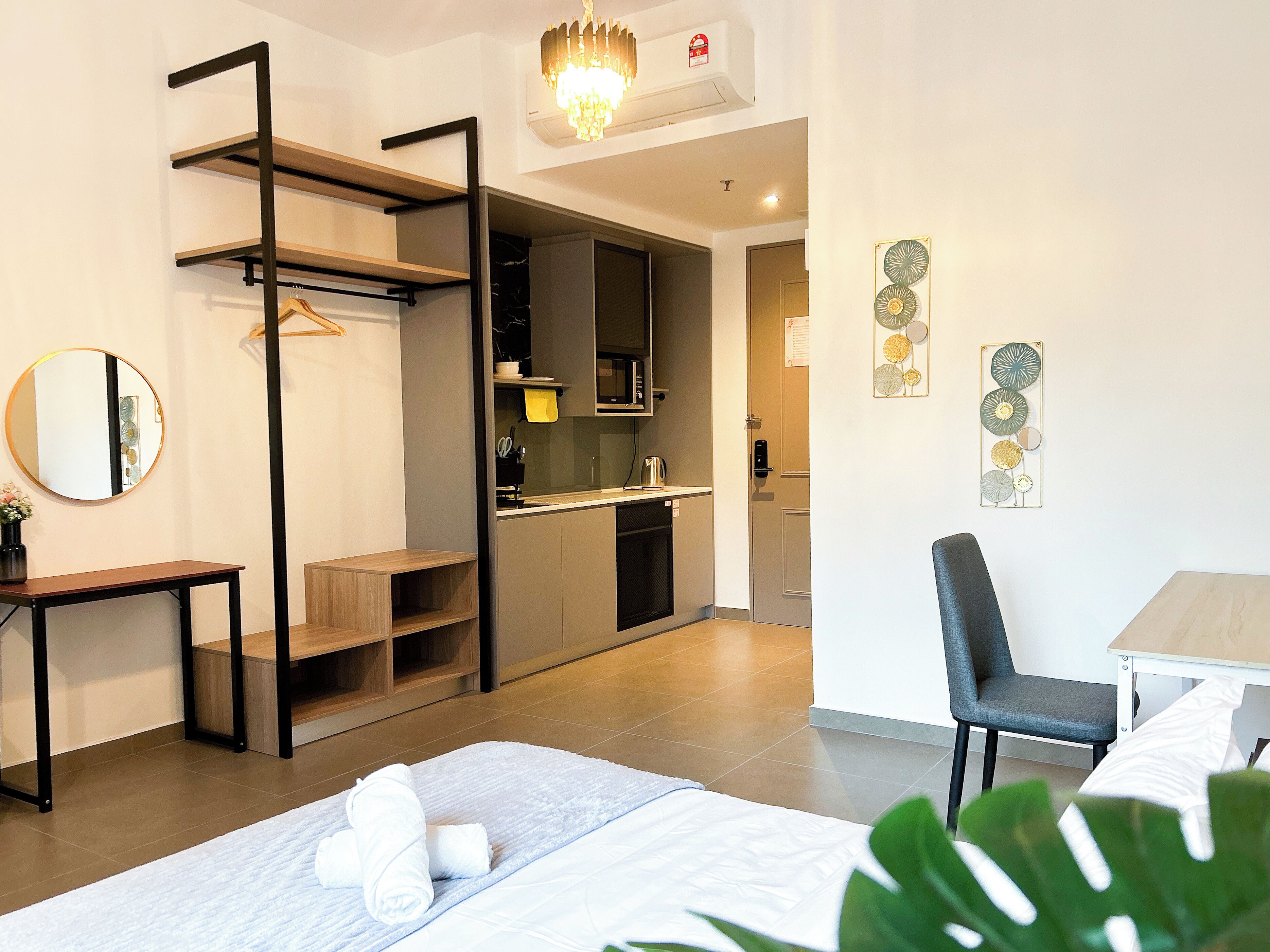 A modern hotel room with a bed, a desk, a chair, a kitchenette, and a bathroom.