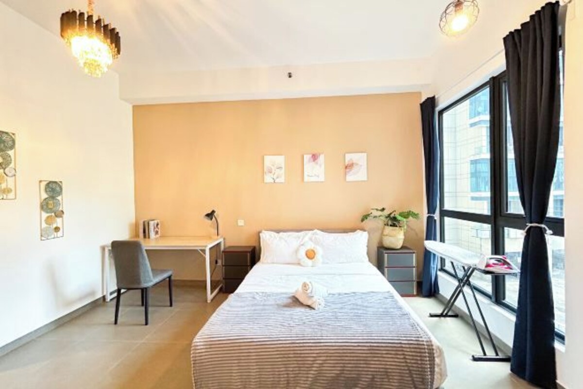 Habitación de hotel con cama, escritorio, silla, mesita y ventana con cortinas.