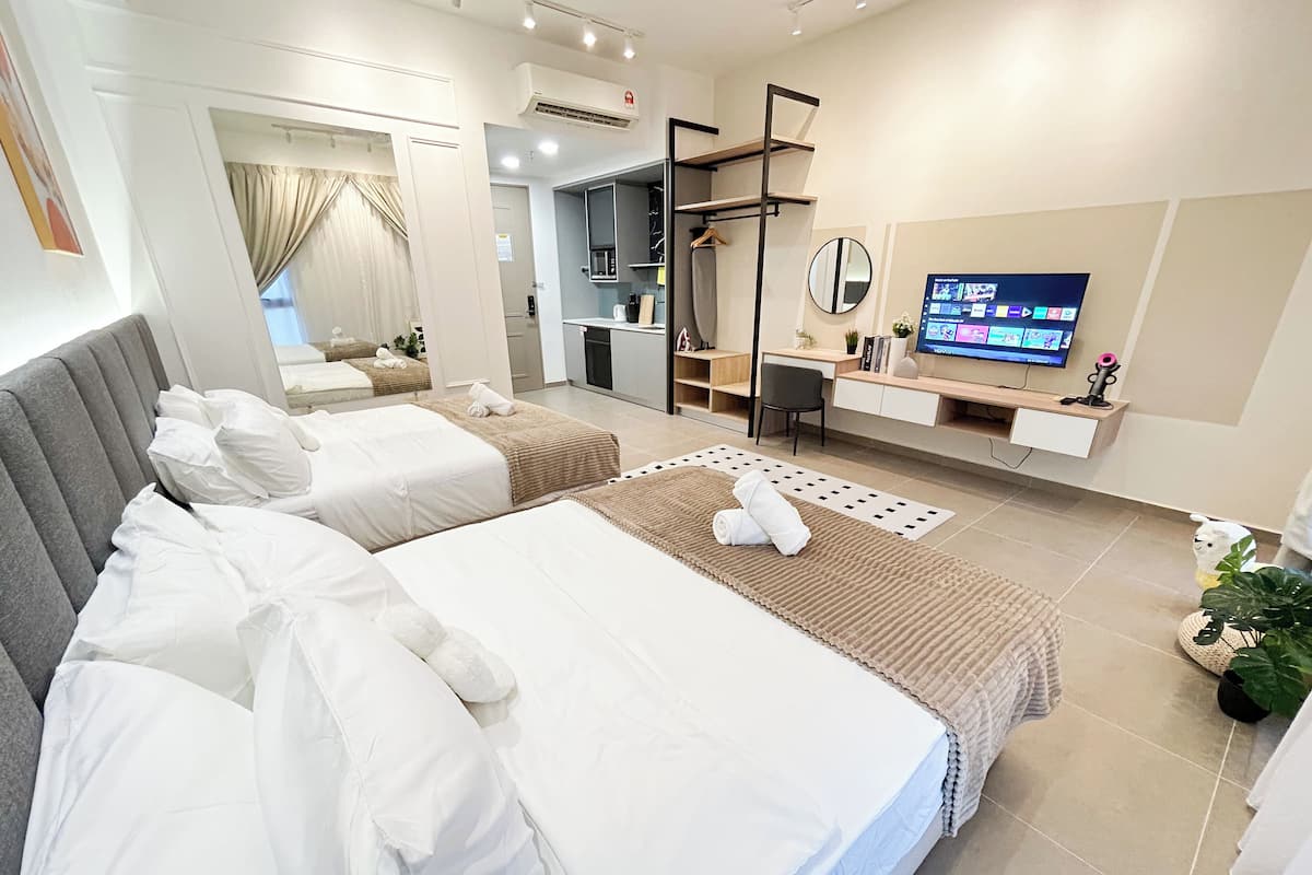 A modern hotel room with two beds, a TV, a desk, and a kitchen area.