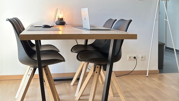 A modern dining area with a wooden table, black chairs, a laptop, and a wall-mounted painting of seagulls over the ocean. - New! Exclusive city apartment - washing machine (Karlsruhe)