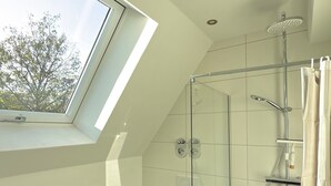 A modern bathroom with a skylight, a glass shower enclosure, a toilet, and a sink. - New! Exclusive city apartment - washing machine (Karlsruhe)