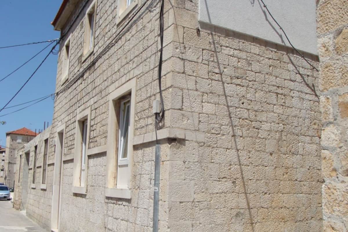 Un edificio de piedra con múltiples ventanas y una caja eléctrica visible en la pared.