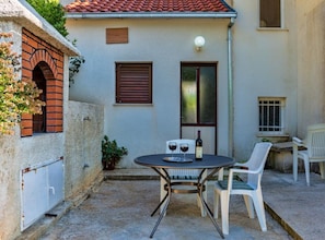 A small outdoor patio with a round table and two chairs, a bottle of wine, and a potted plant.