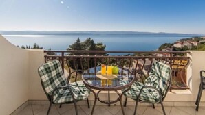 A balcony with wicker chairs and a glass table, overlooking a lake and distant hills. - Apartment Tafra 1 (Omis)
