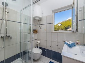 A bathroom with a glass shower enclosure, a toilet, a sink with a window view of a mountain landscape.