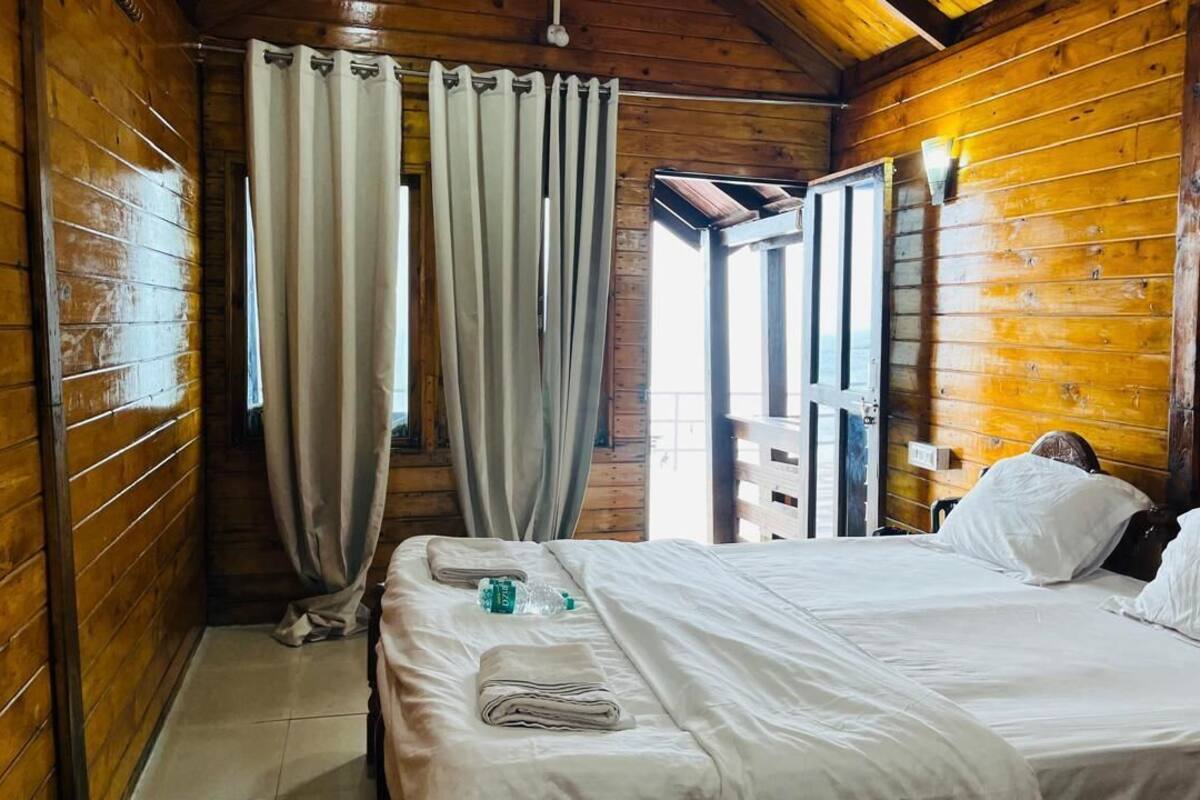 A wooden cabin room with a bed, curtains, and a window.