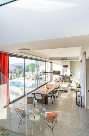 Una sala de estar moderna con un amplio ventanal, un comedor con mesa y sillas de madera, y una cocina al fondo.