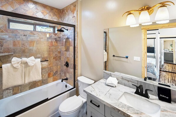 A bathroom with a stone shower, a white toilet, a marble sink, and a large mirror.
