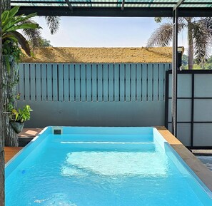 A rectangular swimming pool with a blue interior, surrounded by a wooden deck and a metal fence. - The Son Resort (Pranburi)