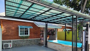 A covered outdoor area with a swimming pool, a stone wall, and a metal gate.