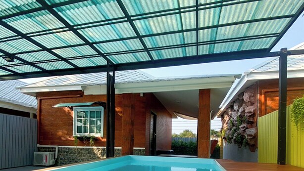 A swimming pool with a glass ceiling, surrounded by a wooden deck and a stone wall.