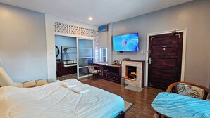 A hotel room with a large bed, a desk with a chair, a television, and a fireplace.