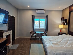 A hotel room with a bed, a desk with two chairs, a TV, a fireplace, and a window with curtains. - The Son Resort (Pranburi)