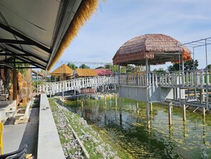 A bridge over a water body with a thatched-roof structure on the right. - The Son Resort (Pranburi)
