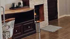A living room with a flat-screen TV mounted on the wall, a fireplace, a wooden coffee table, a patterned armchair, and a dark wooden door.