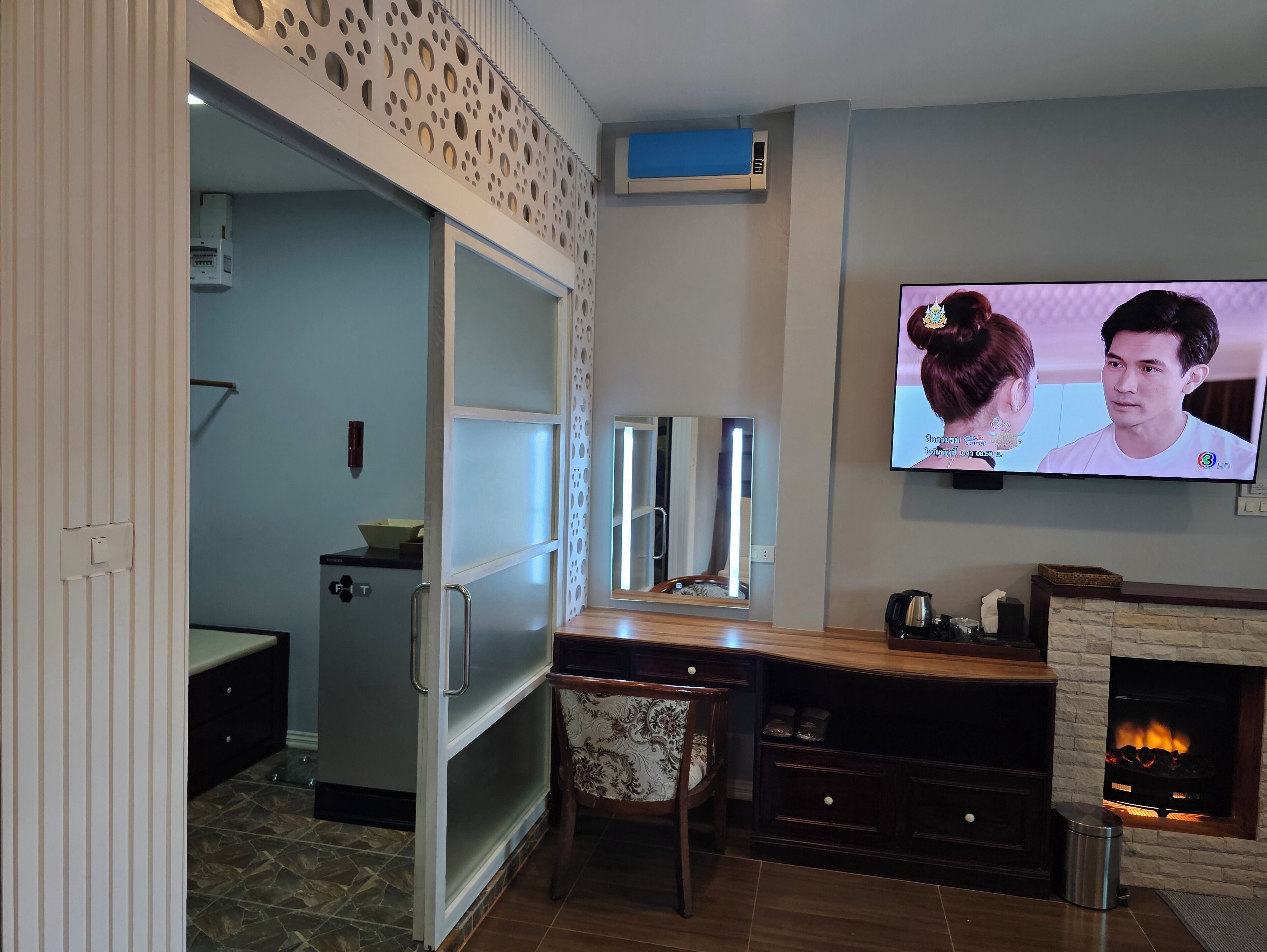 Un salon moderne avec un téléviseur fixé au mur, une cheminée et un coin cuisine visible à travers une porte ouverte.