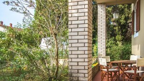Een terras met een bakstenen pilaar, tuinmeubilair en uitzicht op omliggend groen.