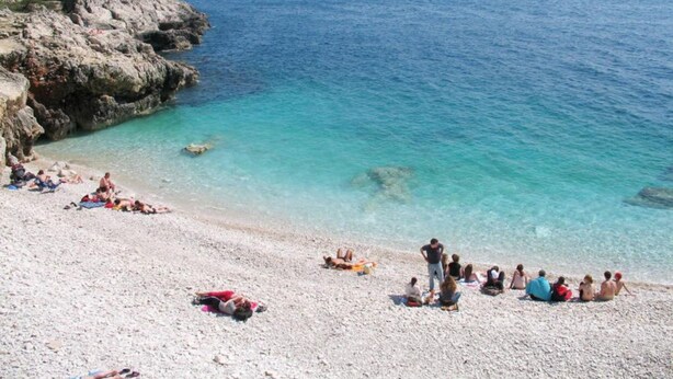 Een strand met helder turquoise water, rotsachtige kliffen en mensen die zonnebaden.
