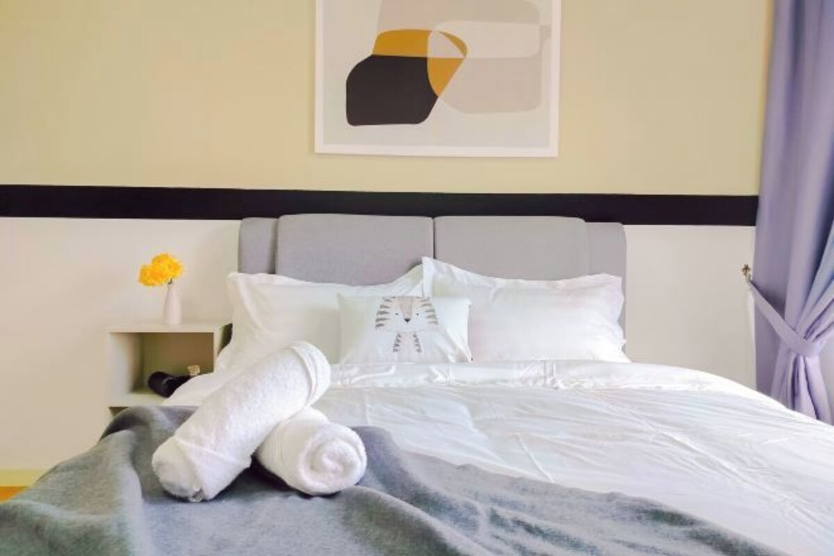 Un lit bien fait, avec des draps blancs, une couverture grise et des serviettes enroulées.