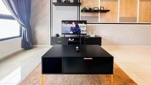 En moderne stue med et fladskærms-tv på et sort stativ, en lille hvid højttaler og en fjernbetjening på stativet.