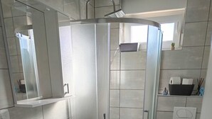 A modern bathroom with a glass-enclosed shower, a built-in washing machine, a sink, and a toilet. - Cozy Apartment Bili (Privlaka)