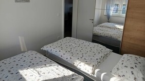 A bedroom with two beds, a wardrobe, and a mirror reflecting the room. - Cozy Apartment Bili (Privlaka)