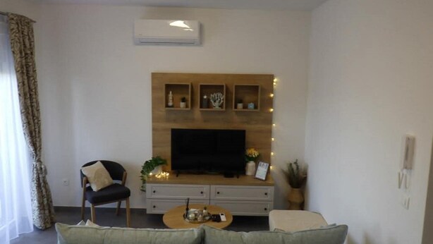 A living room with a sofa, a chair, a coffee table, a TV, and decorative shelves. - Cozy Apartment Bili (Privlaka)