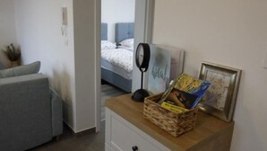 A bedroom with a bed, a bedside table with a lamp, a small cabinet, and a wall-mounted shelf with books and a framed picture. - Cozy Apartment Bili (Privlaka)