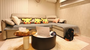 Un salon moderne avec un canapé, un ordinateur portable posé sur une table basse ronde et un jouet en peluche à l’effigie de Pikachu.