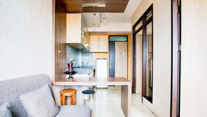 A modern kitchen with a central island, a dining area with a grey sofa, and a hallway leading to a door. - Collection O Apartment By Boboin Baros Near Stasiun Cimahi (Cimahi)