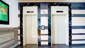An elevator area with two doors labeled "Passenger" and "Service," marble wall designs, and a digital display showing the floor number. - Collection O Apartment By Boboin Baros Near Stasiun Cimahi (Cimahi)