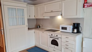 Een kleine keuken met witte kastjes, een magnetron, een koffiezetapparaat en een fornuis.