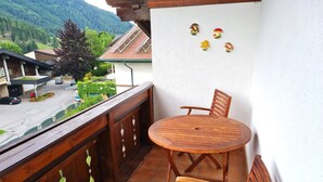 Een balkon met een houten tafel en stoelen, uitzicht op een weg en een berg op de achtergrond.